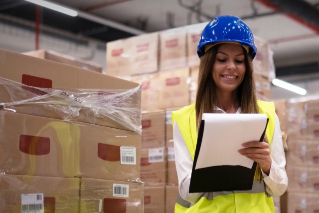 person writing on clipboard in front of stacks of boxes