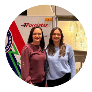 Two women stand side by side in front of a Purolator delivery e-bike, one wearing a burgundy long‑sleeve blouse and the other a light blue sweater. The graphic reads “International Women’s Day” and includes the quote: “As a young engineer woman in logistics, I had mentors that supported me and encouraged me to keep going.” Purolator branding appears below the quote.