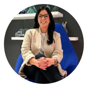 A woman wearing a beige jacket, black pants and glasses sits in a modern blue chair inside an office setting with her legs crossed and hands folded on her knee. “International Women’s Day” appears at the top of the graphic, along with the quote: “Giving my time through mentorship has provided a deep sense of purpose and connection.” Purolator branding is shown at the bottom below the quote.