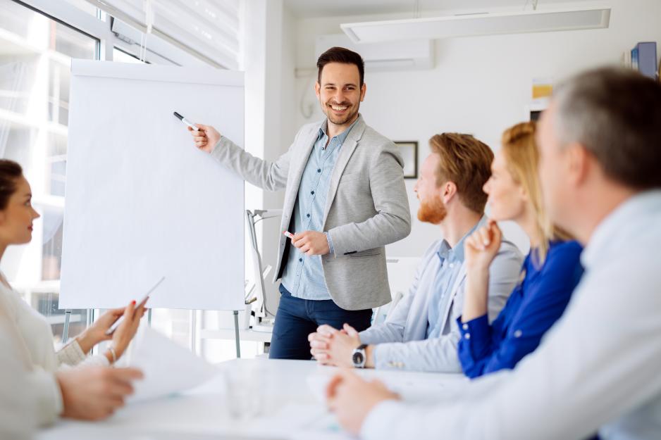 un homme pointant un marqueur sur un tableau blanc pendant que l'équipe regarde