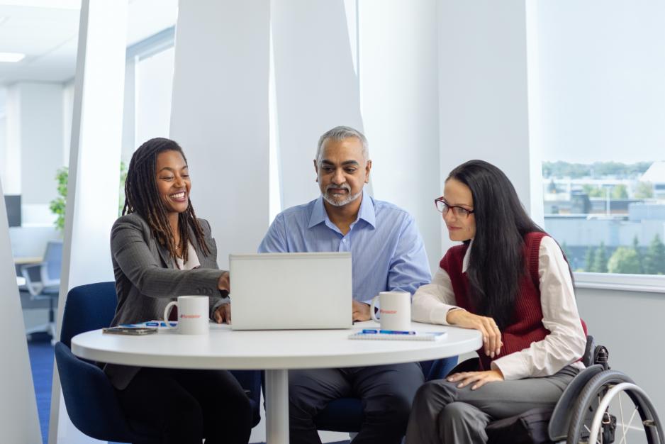 3 people sitting around a table, looking at a laptop